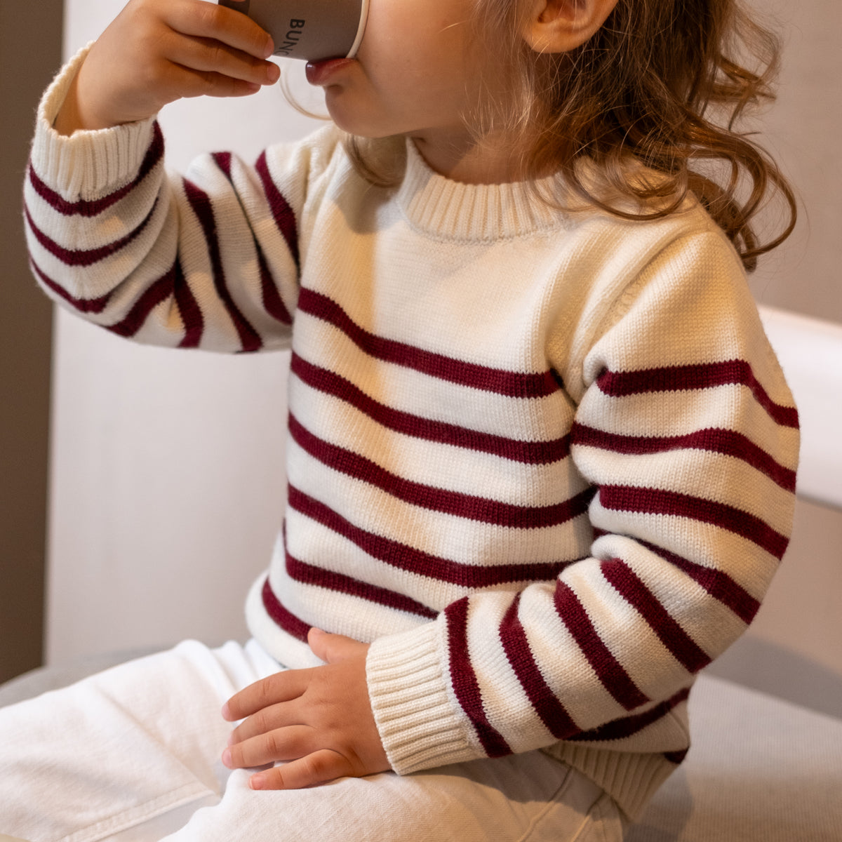 Little girl wearing Breton striped nautical inspired wool sweater in off white and dark red 